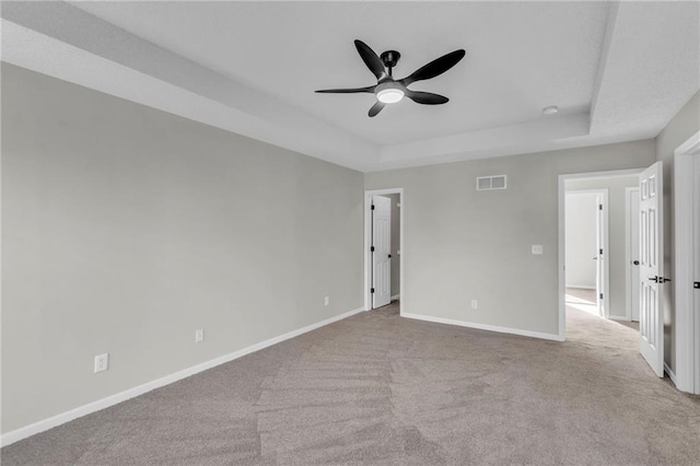 empty room featuring a raised ceiling, light carpet, and ceiling fan