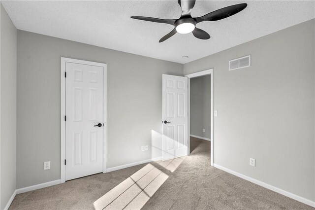 unfurnished bedroom with ceiling fan, light colored carpet, and a textured ceiling