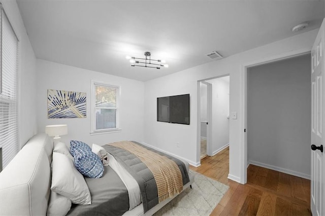 bedroom featuring visible vents, a notable chandelier, baseboards, and wood finished floors