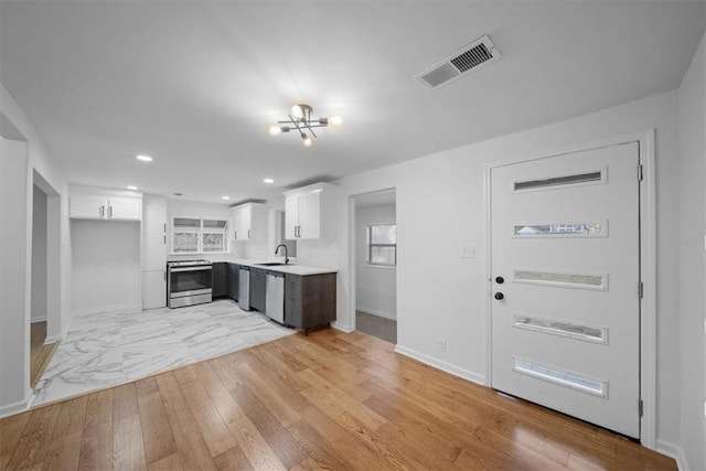 kitchen featuring stainless steel appliances, a sink, visible vents, white cabinets, and light wood finished floors