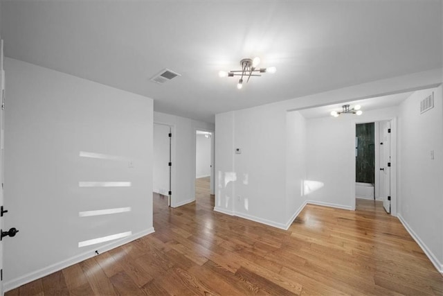 spare room with light wood-style floors, visible vents, and an inviting chandelier