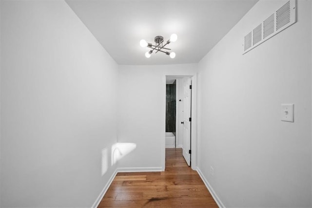 hallway featuring baseboards, wood finished floors, visible vents, and a notable chandelier