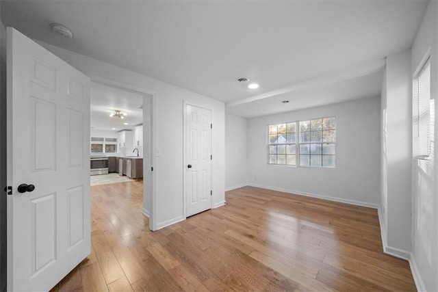 spare room with light wood-style floors, a sink, and baseboards