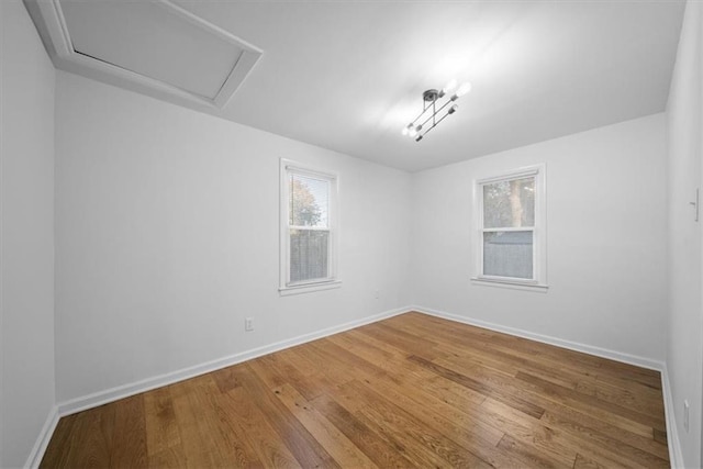 unfurnished room featuring attic access, baseboards, and wood finished floors