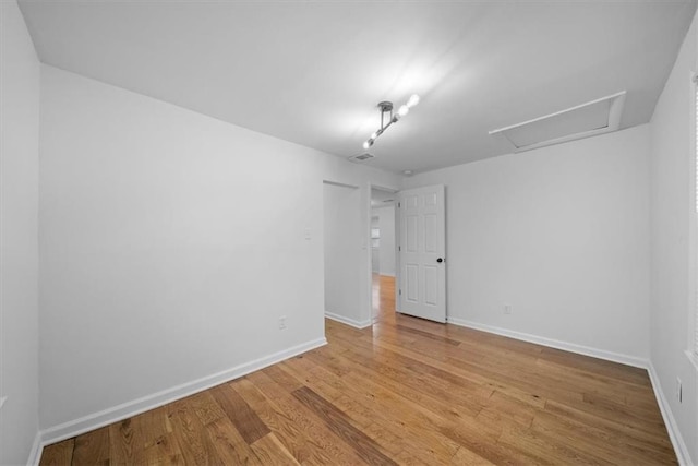 spare room with attic access, visible vents, light wood-style floors, and baseboards