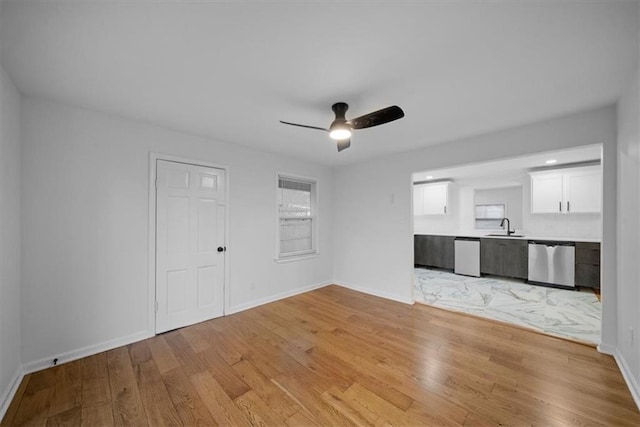 unfurnished living room featuring a ceiling fan, baseboards, a sink, and light wood finished floors