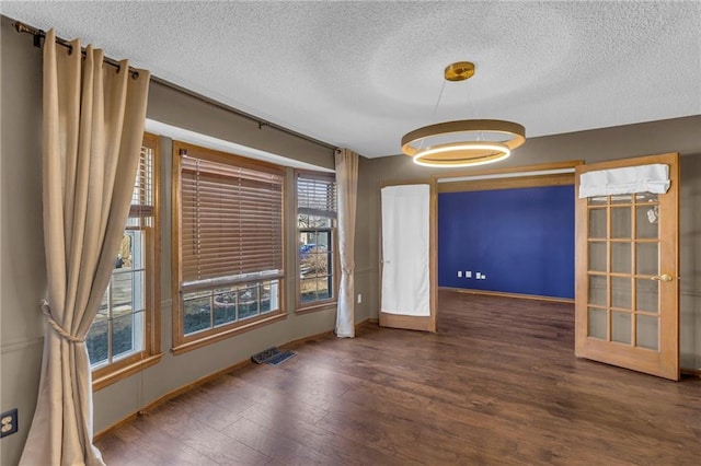 unfurnished room with a textured ceiling, baseboards, wood finished floors, and french doors