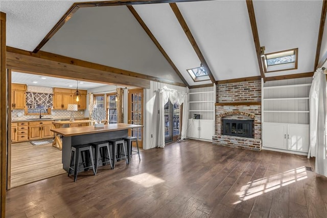 kitchen featuring vaulted ceiling with skylight, a fireplace, a sink, and hardwood / wood-style flooring