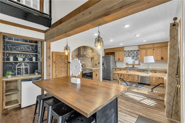 kitchen with arched walkways, stainless steel appliances, butcher block counters, wood finished floors, and tasteful backsplash