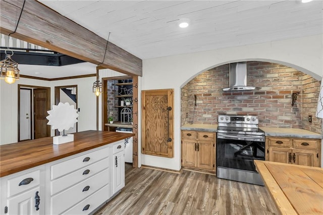 kitchen with brick wall, wood finished floors, wooden counters, stainless steel electric stove, and wall chimney exhaust hood