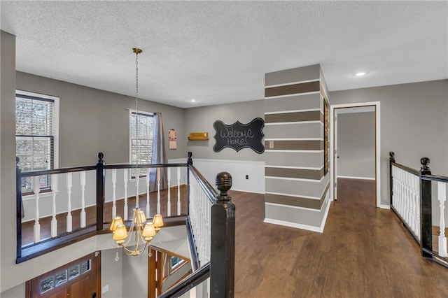 hallway with a textured ceiling, a notable chandelier, wood finished floors, an upstairs landing, and baseboards