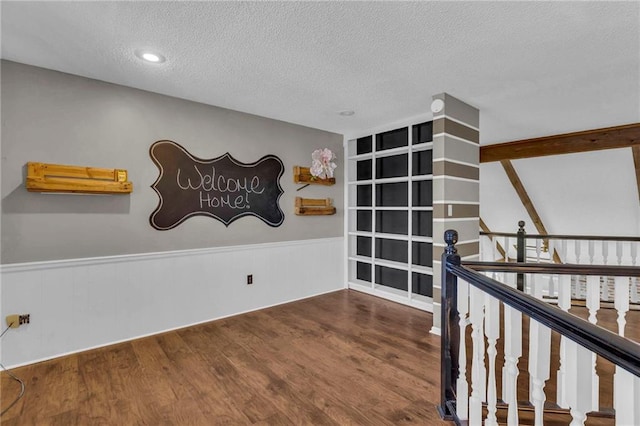 interior space featuring a wainscoted wall, a textured ceiling, wood finished floors, and an upstairs landing