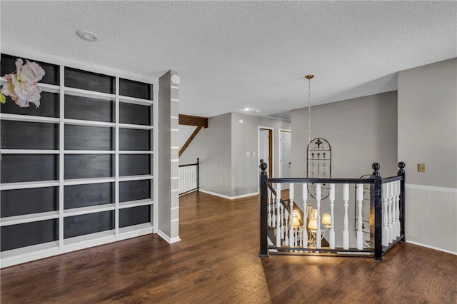 corridor featuring a textured ceiling, wood finished floors, an upstairs landing, and a notable chandelier