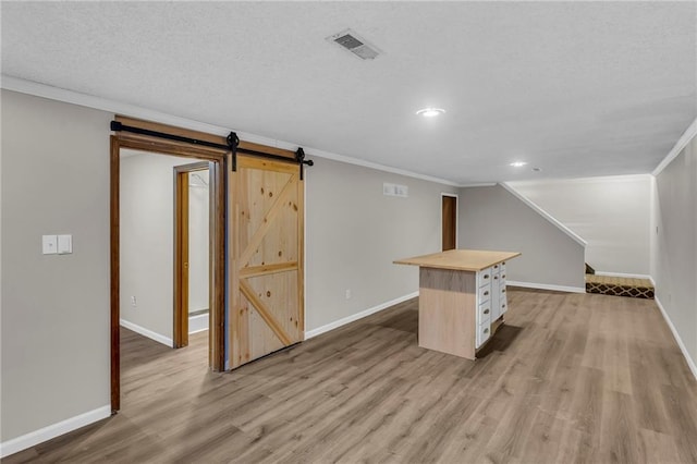 interior space with light wood-type flooring, visible vents, baseboards, and a barn door