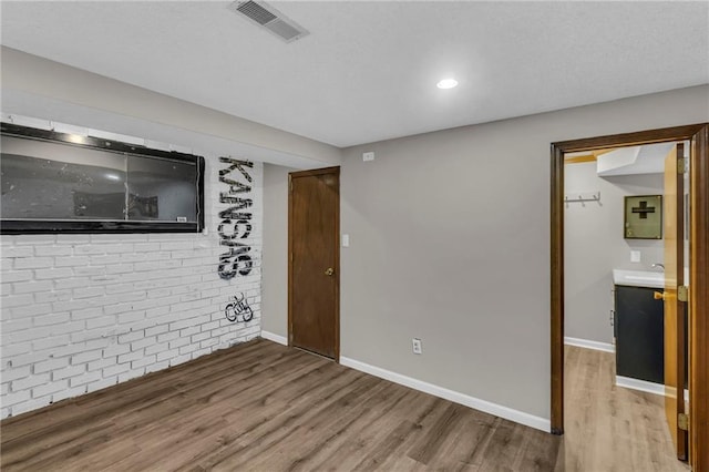 empty room featuring light wood finished floors, brick wall, visible vents, and baseboards