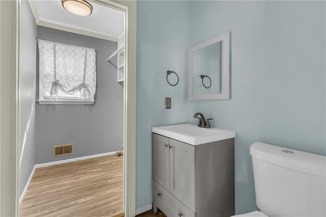 bathroom with visible vents, toilet, vanity, wood finished floors, and baseboards