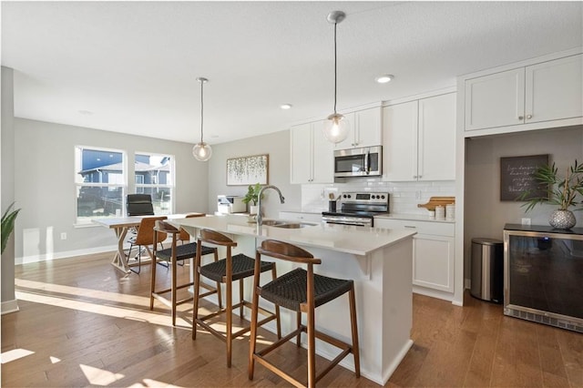 kitchen with white cabinets, pendant lighting, stainless steel appliances, and a kitchen island with sink