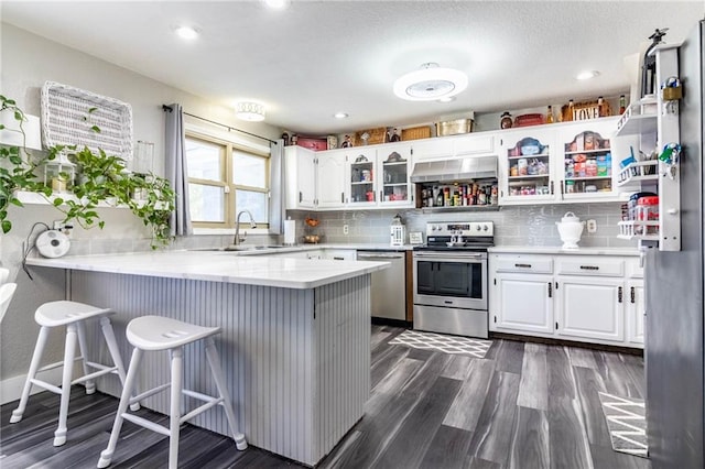 kitchen featuring kitchen peninsula, dark hardwood / wood-style floors, a kitchen bar, white cabinetry, and stainless steel appliances