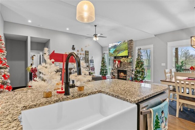 kitchen with light wood-type flooring, ceiling fan, sink, pendant lighting, and a stone fireplace