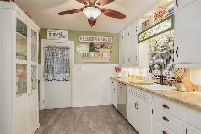 kitchen featuring white cabinetry, dishwasher, ceiling fan, sink, and wooden walls