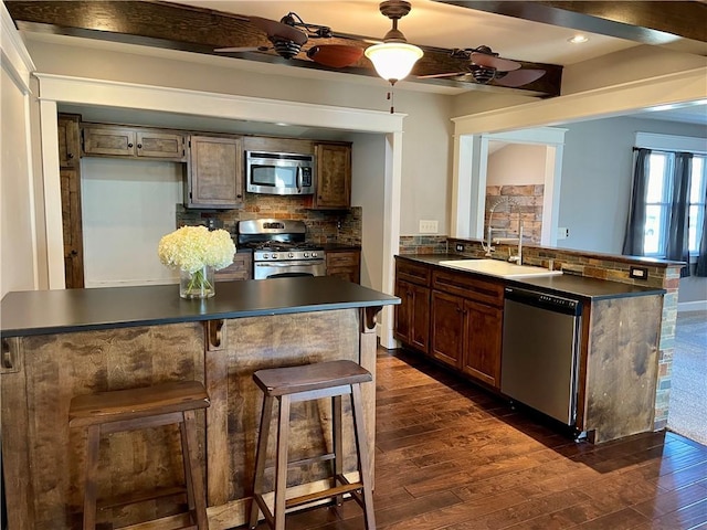 kitchen with dark countertops, appliances with stainless steel finishes, a peninsula, and dark wood finished floors