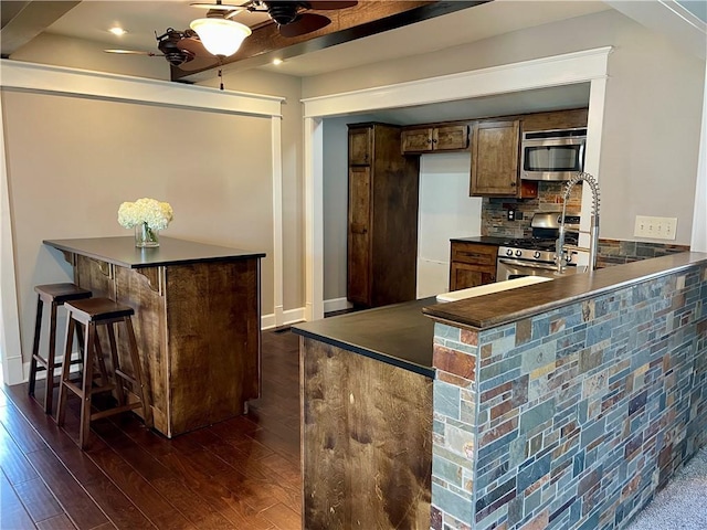 kitchen featuring dark countertops, a peninsula, dark wood-style floors, stainless steel appliances, and a ceiling fan