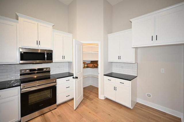 kitchen featuring white cabinetry, decorative backsplash, a high ceiling, stainless steel appliances, and light wood-type flooring