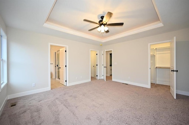 unfurnished bedroom with a walk in closet, ceiling fan, a raised ceiling, light carpet, and ensuite bath