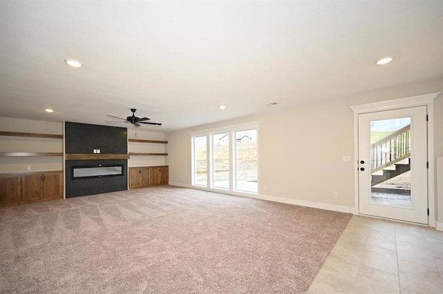 unfurnished living room with ceiling fan, a large fireplace, and light colored carpet