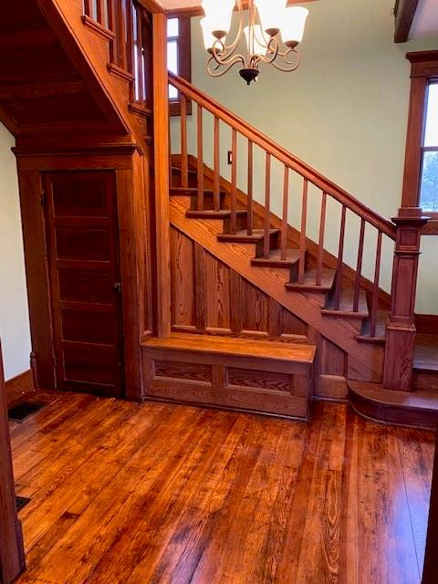 stairs with hardwood / wood-style floors, wood walls, and an inviting chandelier