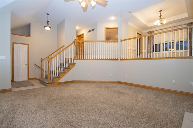 empty room featuring carpet, ceiling fan with notable chandelier, and a tray ceiling