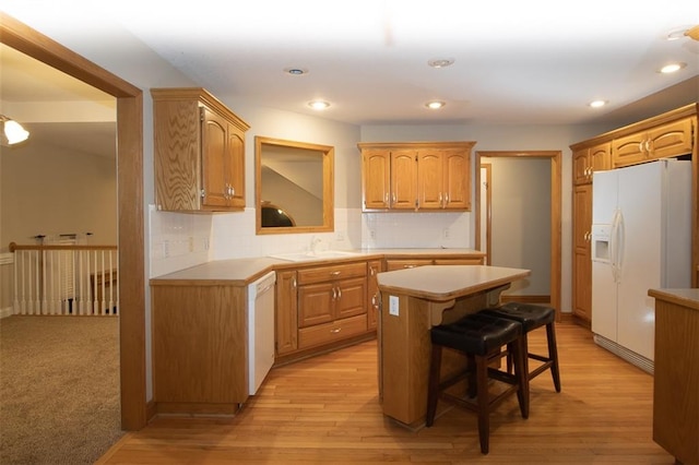 kitchen with tasteful backsplash, white appliances, a kitchen bar, a kitchen island, and light wood-type flooring