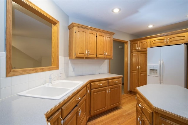 kitchen with backsplash, light wood-type flooring, white fridge with ice dispenser, and sink