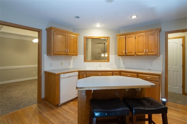 kitchen with sink, backsplash, white dishwasher, light hardwood / wood-style floors, and a breakfast bar