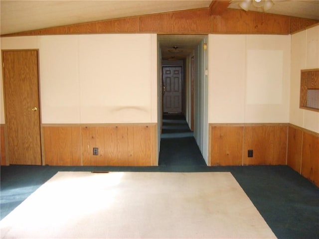 carpeted empty room featuring lofted ceiling and wooden walls