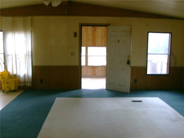 carpeted spare room with vaulted ceiling, plenty of natural light, and wooden walls