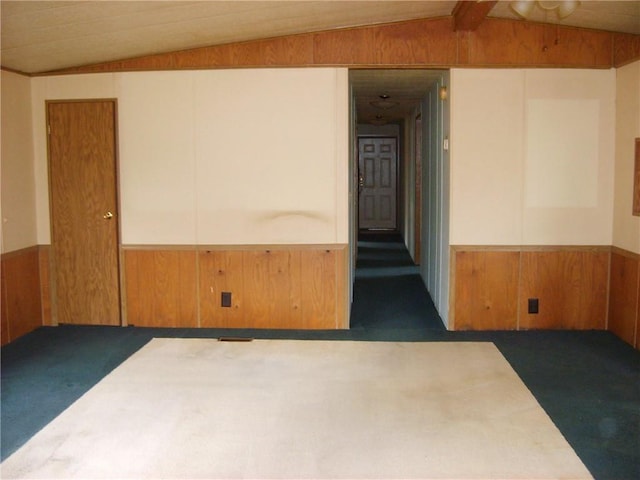 unfurnished room with dark colored carpet, wood walls, and lofted ceiling