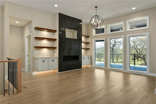 unfurnished living room with light wood-type flooring, a fireplace, a wealth of natural light, and an inviting chandelier