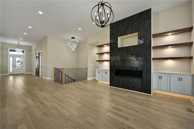 unfurnished living room featuring a fireplace, light hardwood / wood-style flooring, a chandelier, and french doors