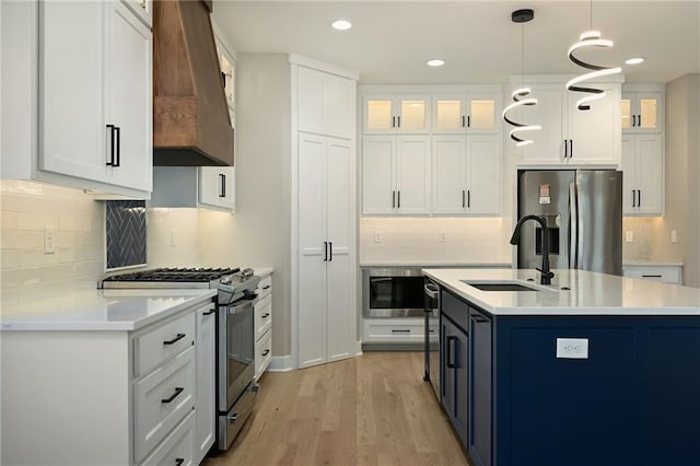 kitchen featuring appliances with stainless steel finishes, premium range hood, decorative light fixtures, light hardwood / wood-style flooring, and white cabinets