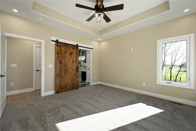 unfurnished bedroom featuring carpet flooring, a barn door, a tray ceiling, and ceiling fan