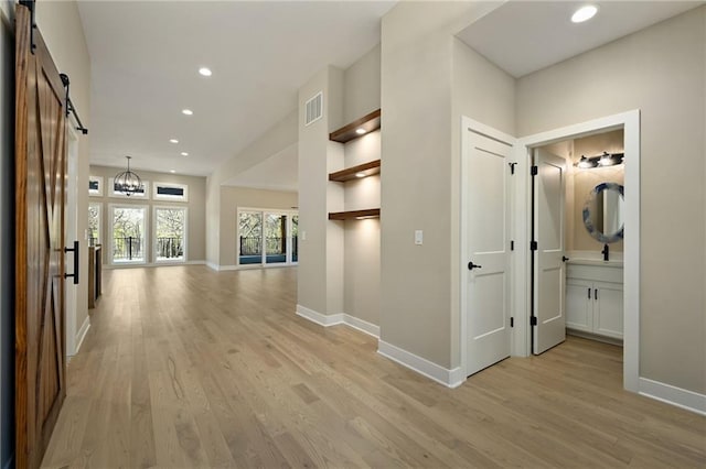 corridor featuring a barn door, light hardwood / wood-style floors, and a notable chandelier