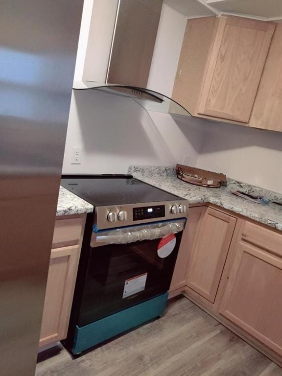 kitchen featuring stainless steel electric range, light brown cabinets, light wood-type flooring, range hood, and light stone counters