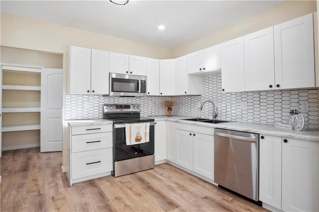 kitchen featuring appliances with stainless steel finishes, tasteful backsplash, sink, white cabinets, and light hardwood / wood-style floors