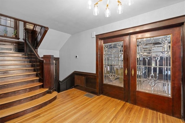 interior space with visible vents, a wainscoted wall, wood finished floors, stairs, and french doors