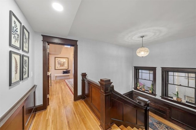 corridor with light wood finished floors, an upstairs landing, and an inviting chandelier