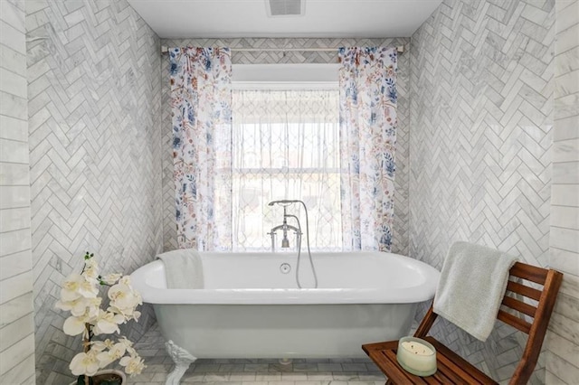 bathroom with a freestanding tub, visible vents, and tile walls