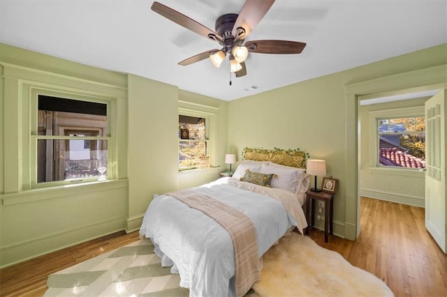 bedroom with light wood-style floors, multiple windows, ceiling fan, and baseboards