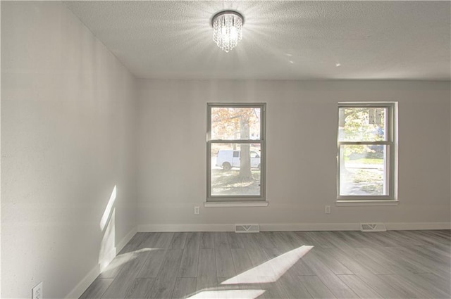 spare room featuring a textured ceiling, light hardwood / wood-style floors, and a notable chandelier