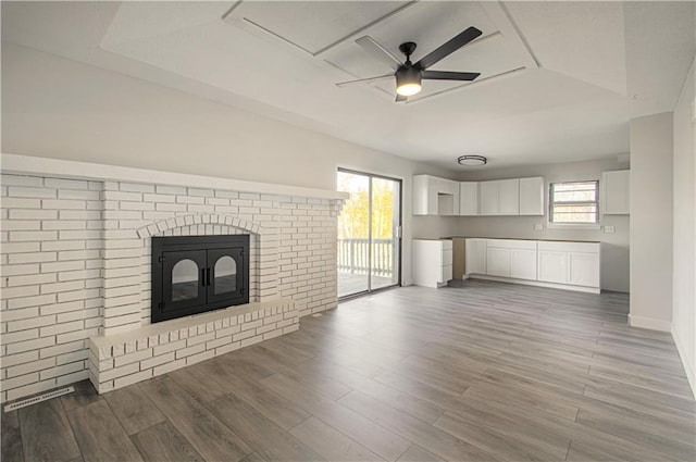 unfurnished living room with a fireplace, hardwood / wood-style flooring, ceiling fan, and a tray ceiling